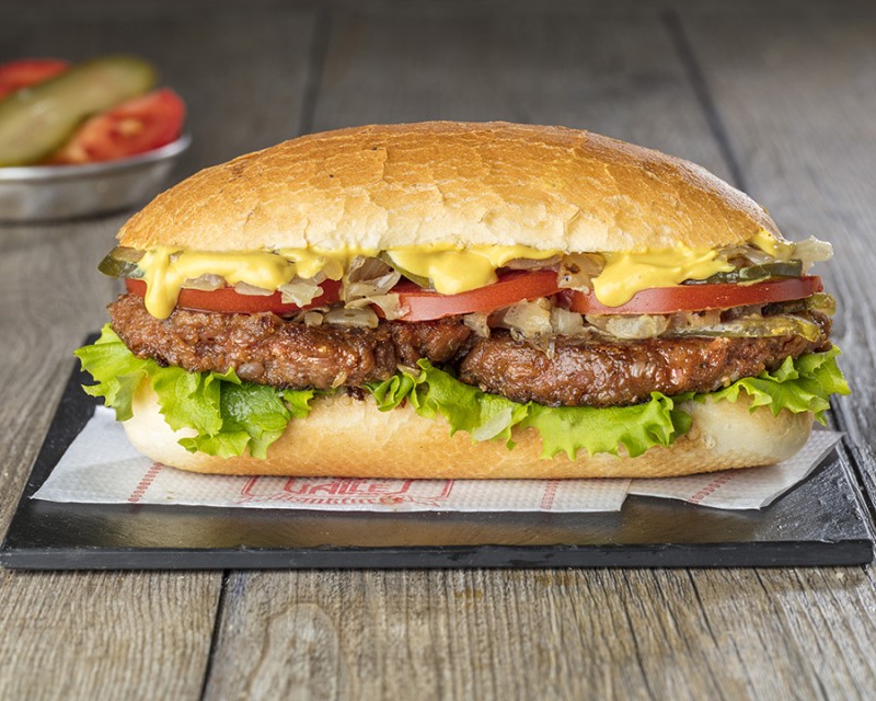 Sugerencia de presentación de un bocadillo de hamburguesa con queso, lechuga, cebolla caramelizada y tomate con salsa de mostaza